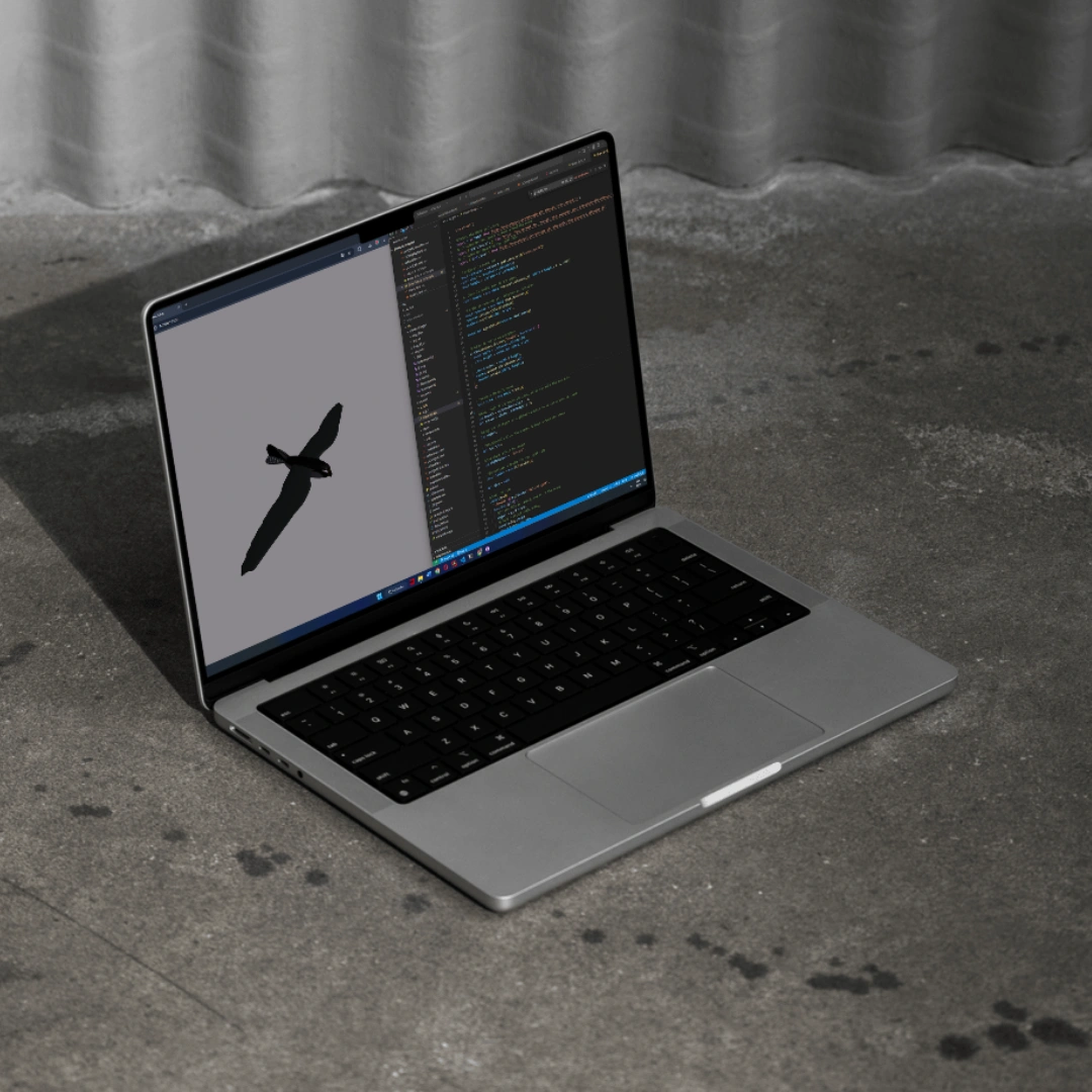 Mock-up montrant un ordinateur posé sur une dalle en béton. L'écran est séparé en deux parties égales (splitscreen), à gauche le rendu de l'oiseu animé avec ThreeJS, et à droite le code.