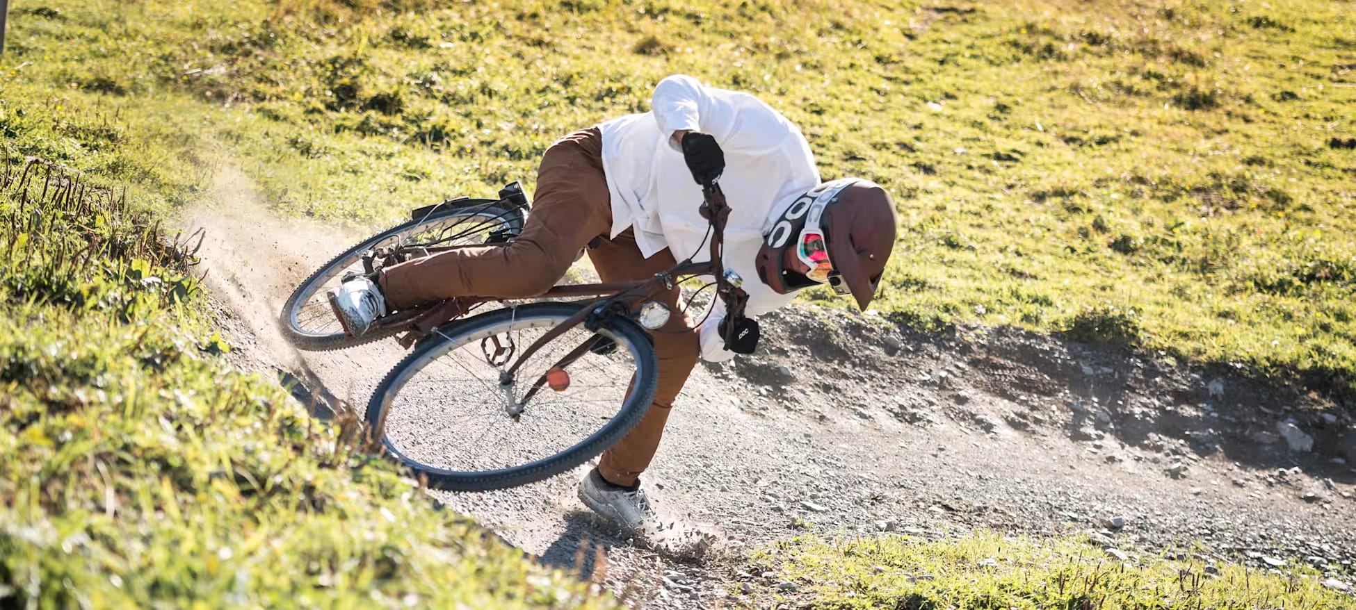 Fabio prenant un virage d'une piste normallement réservée aux VTT, sur vélo de ville.  Il n'a pas ses vêtements de protection habituels (si ce n'est son casque et son masque pour se protéger des poussières), mais porte une chemise et un jeans brun